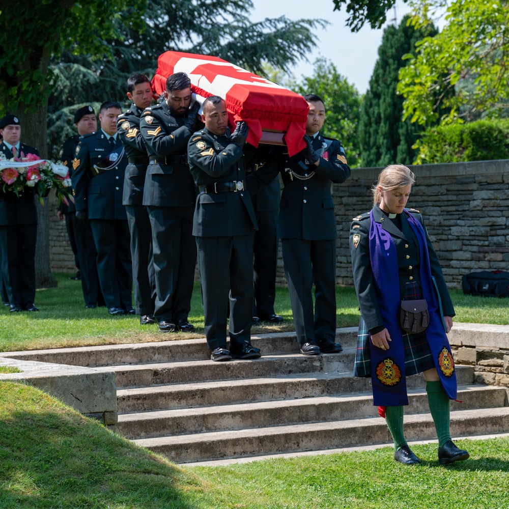 Une célébrante marche. Derrière elle, les soldats portant le cercueil descendent des escaliers menant au cimetière.