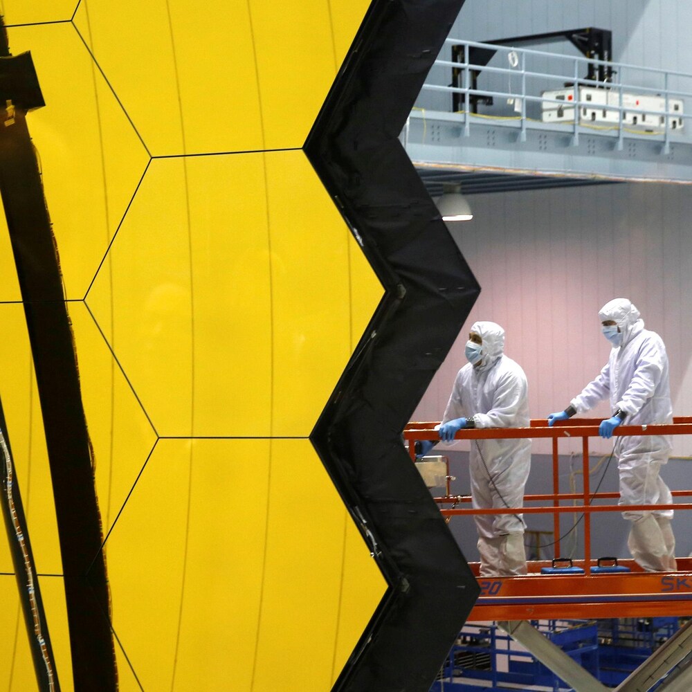 Des travailleurs en combinaison près d'un télescope spatial.