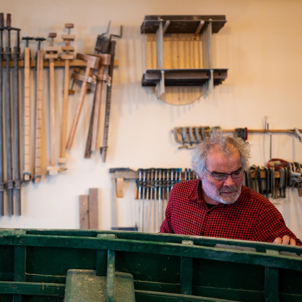 Daniel St-Pierre dans un atelier, des outils accrochés sur le mur derrière lui alors qu'il regarde une chaloupe. 