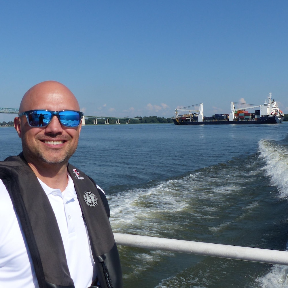 Le pilote François Fugère sur le fleuve avec le cargo Sedna en arrière-plan près de Trois-Rivières.