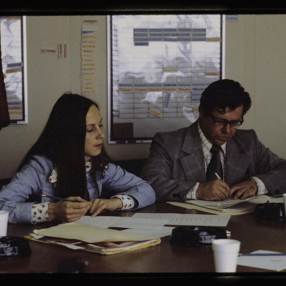 un homme et une femme assis à une table de travail avec feuilles devant eux.