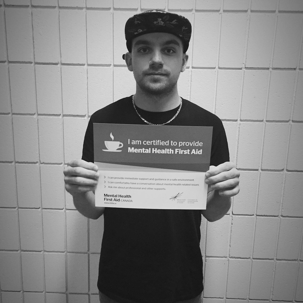 Un homme tient une affiche qui affirme « I am certified to provide mental health first aid »