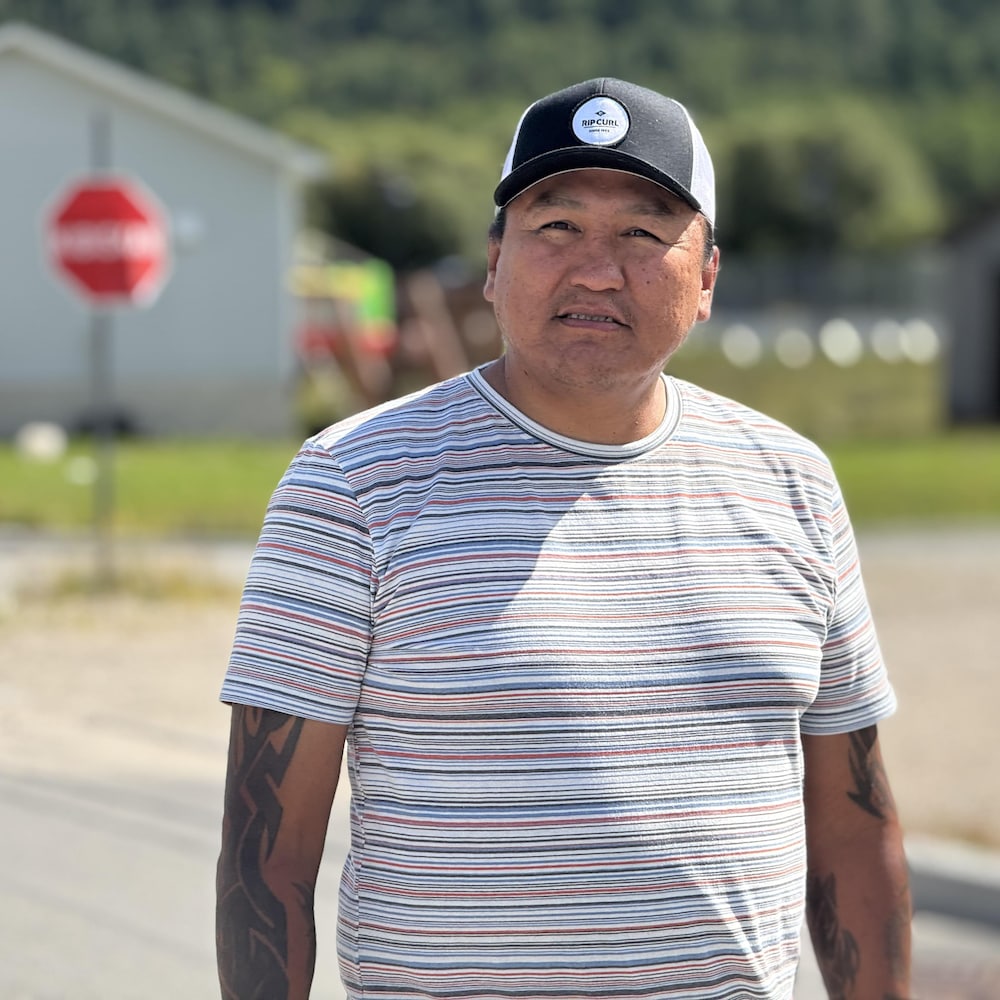 Un homme coiffé d’une casquette se tient dans une rue de Winneway, devant des maisons de la communauté.