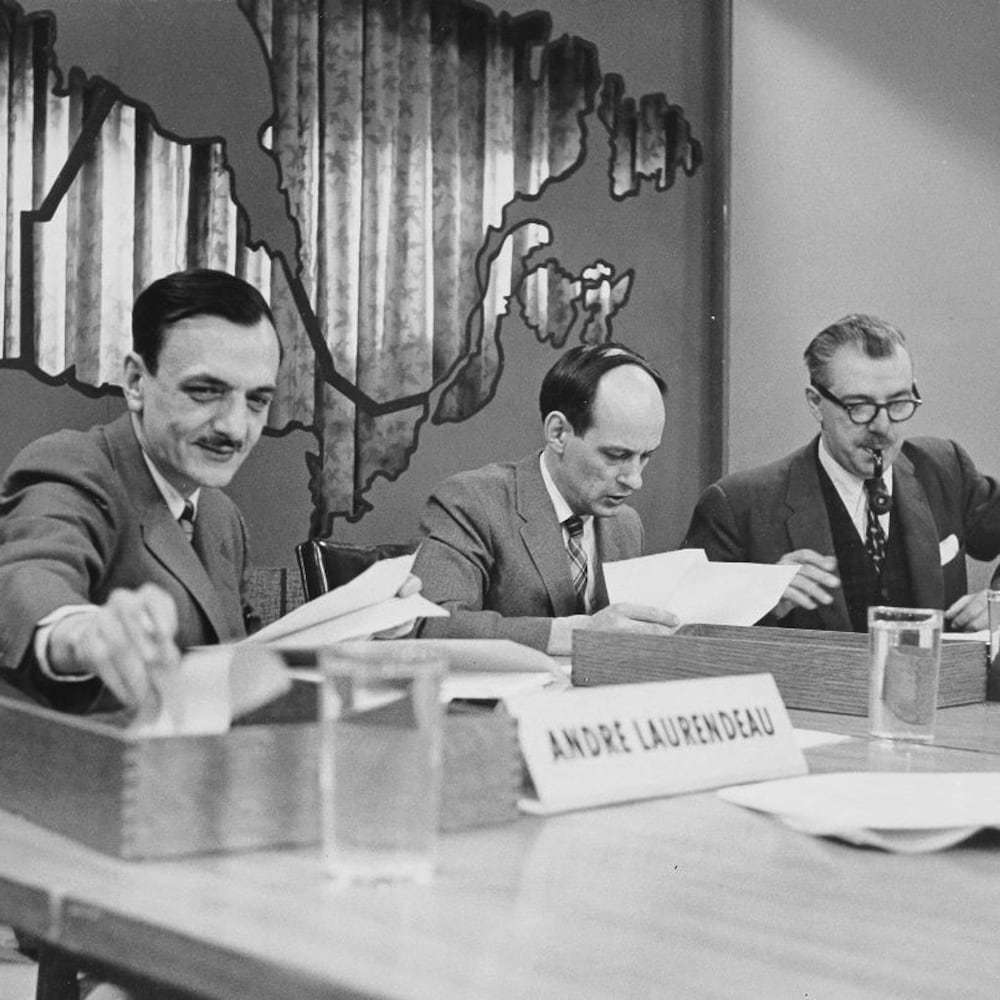 André Laurendeau, René Lévesque et Roger Duhamel consultant leurs notes sur un long bureau.
