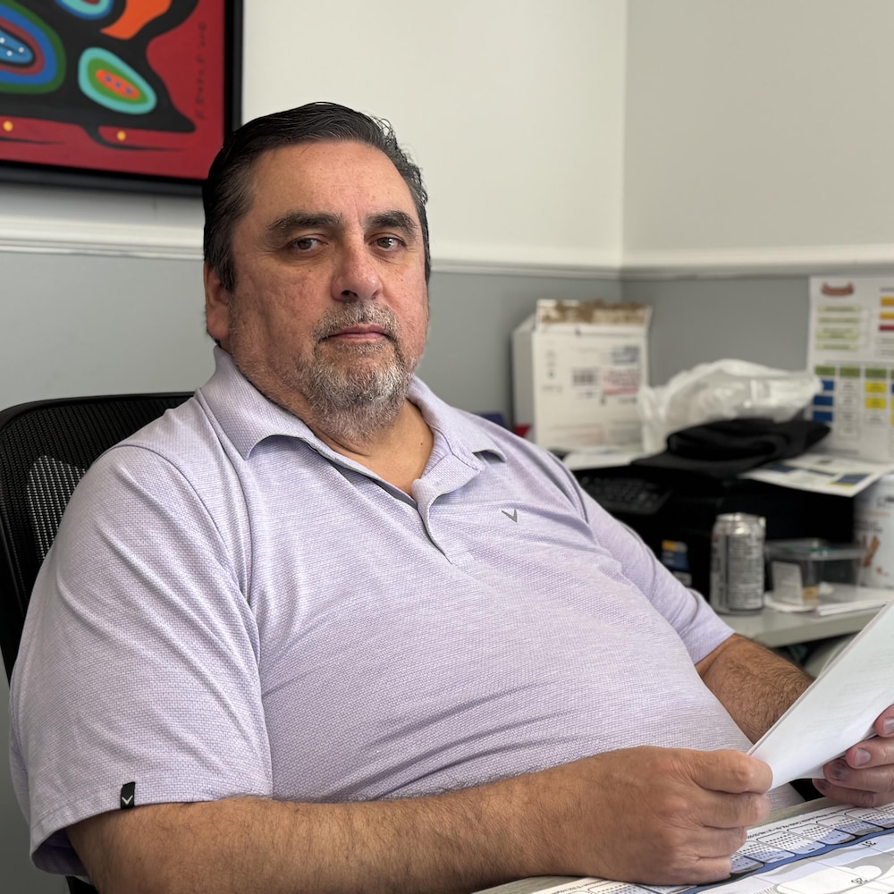 Un homme assis à son bureau tient des documents entre ses mains, sous une œuvre aux couleurs vives.