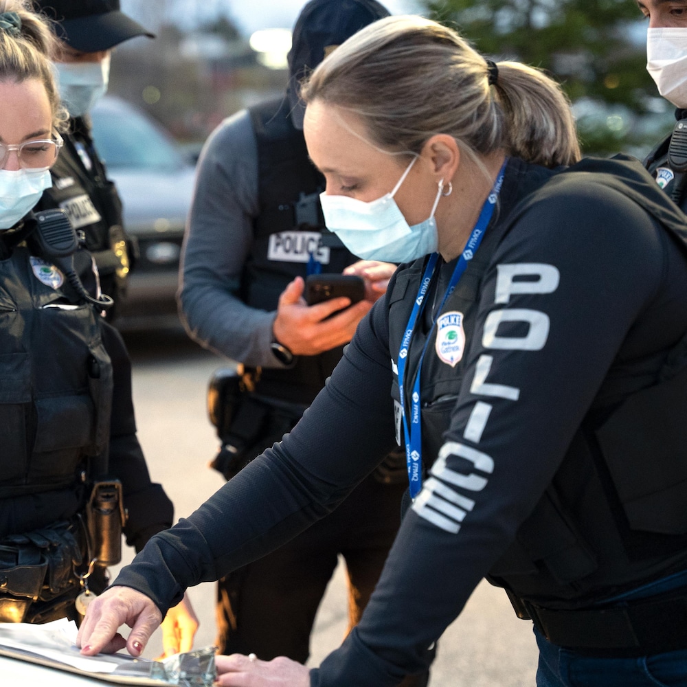 Deux policières vêtues de gilets pare-balles regardent une feuille de papier sur le capot d'une voiture.
