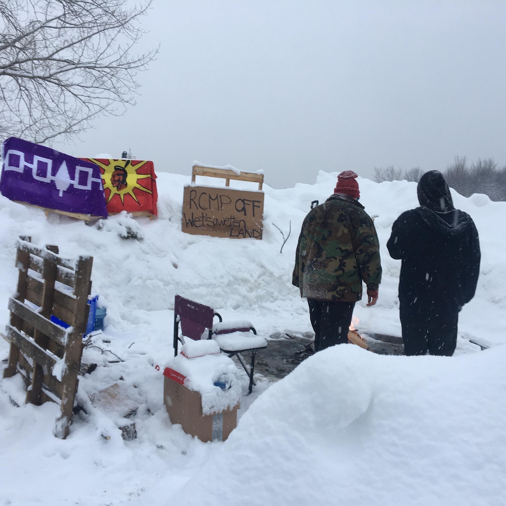 Un drapeau mohawk planté dans un banc de neige où se tiennent deux personnes.