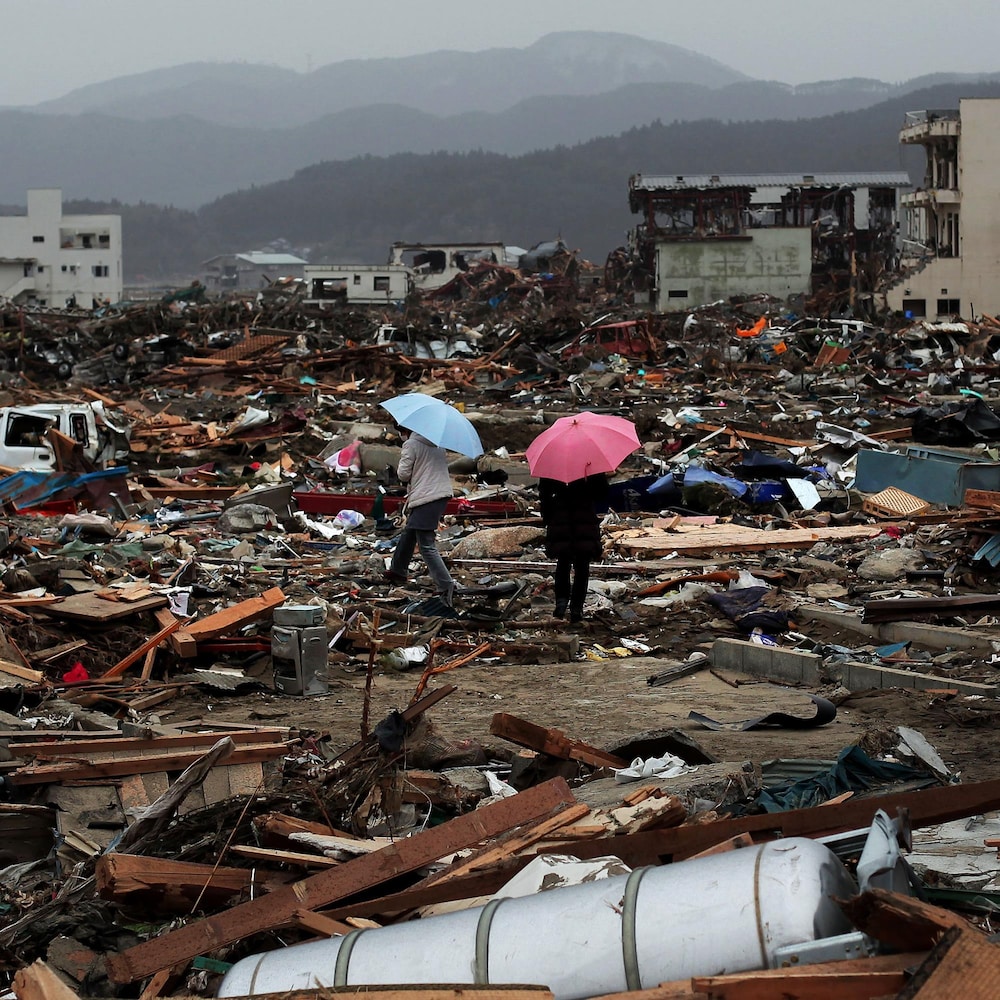 Deux personnes avec des parapluies parmi les décombres du tsunami.