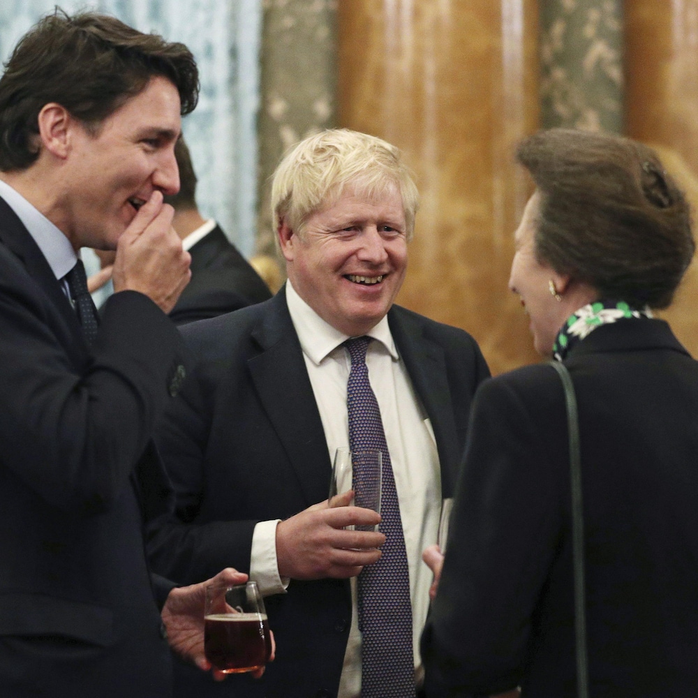 Justin Trudeau, Boris Johnson et la princesse Anne, un verre à la main, conversent en riant.