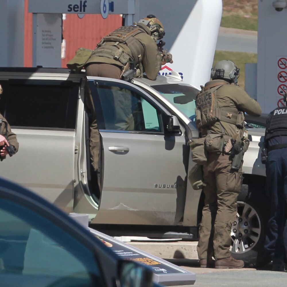 Quatre policiers derrière un véhicule, pointant leurs armes.