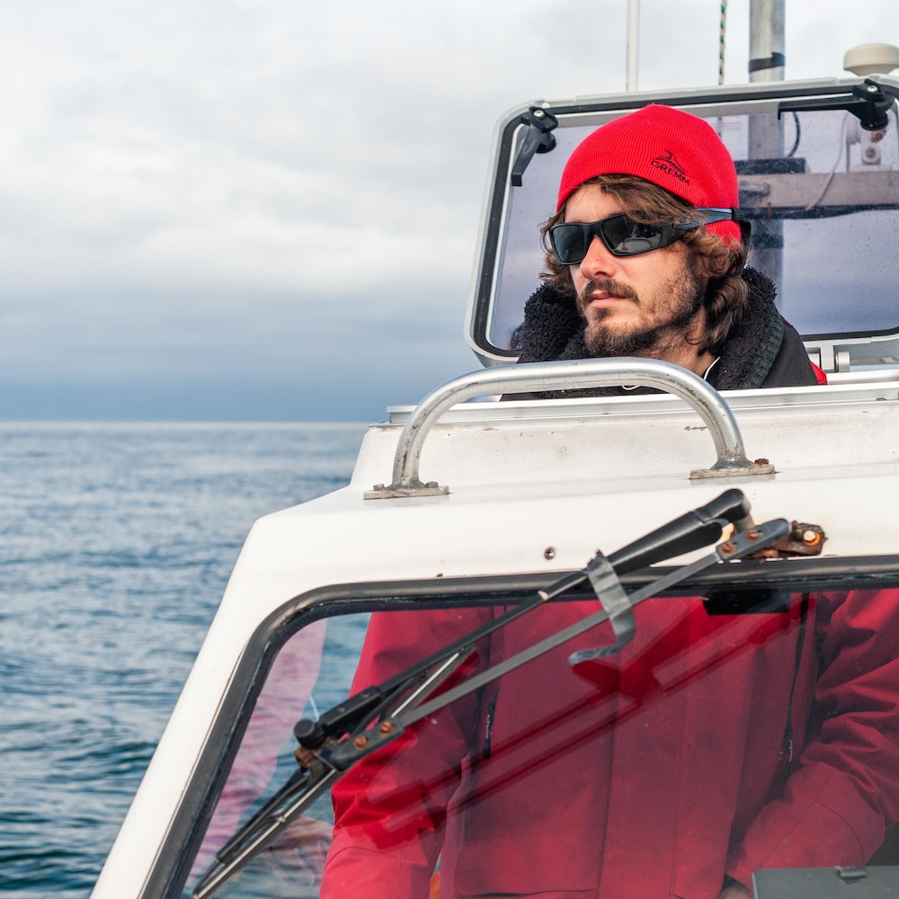 Un homme, vêtu de rouge, scrute l'horizon à la barre du bateau.