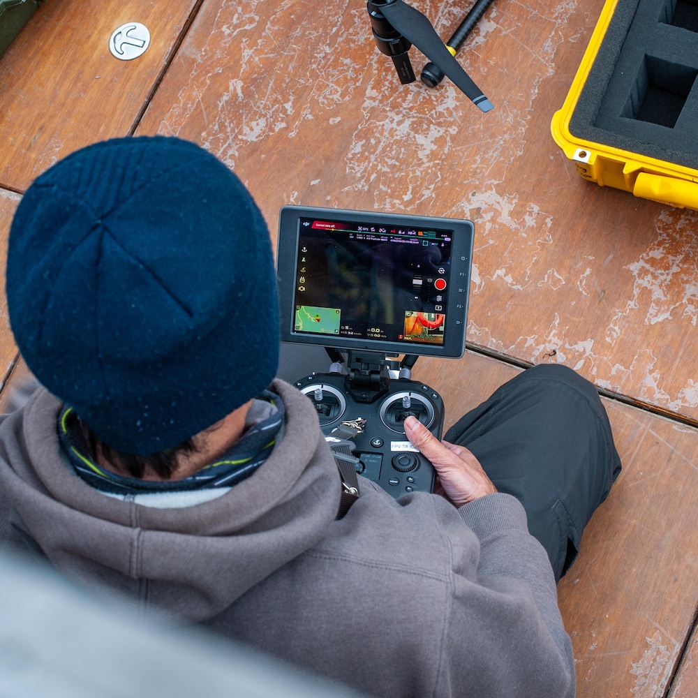 Un homme assis sur le plancher du cockpit prépare la console de contrôle du drone.