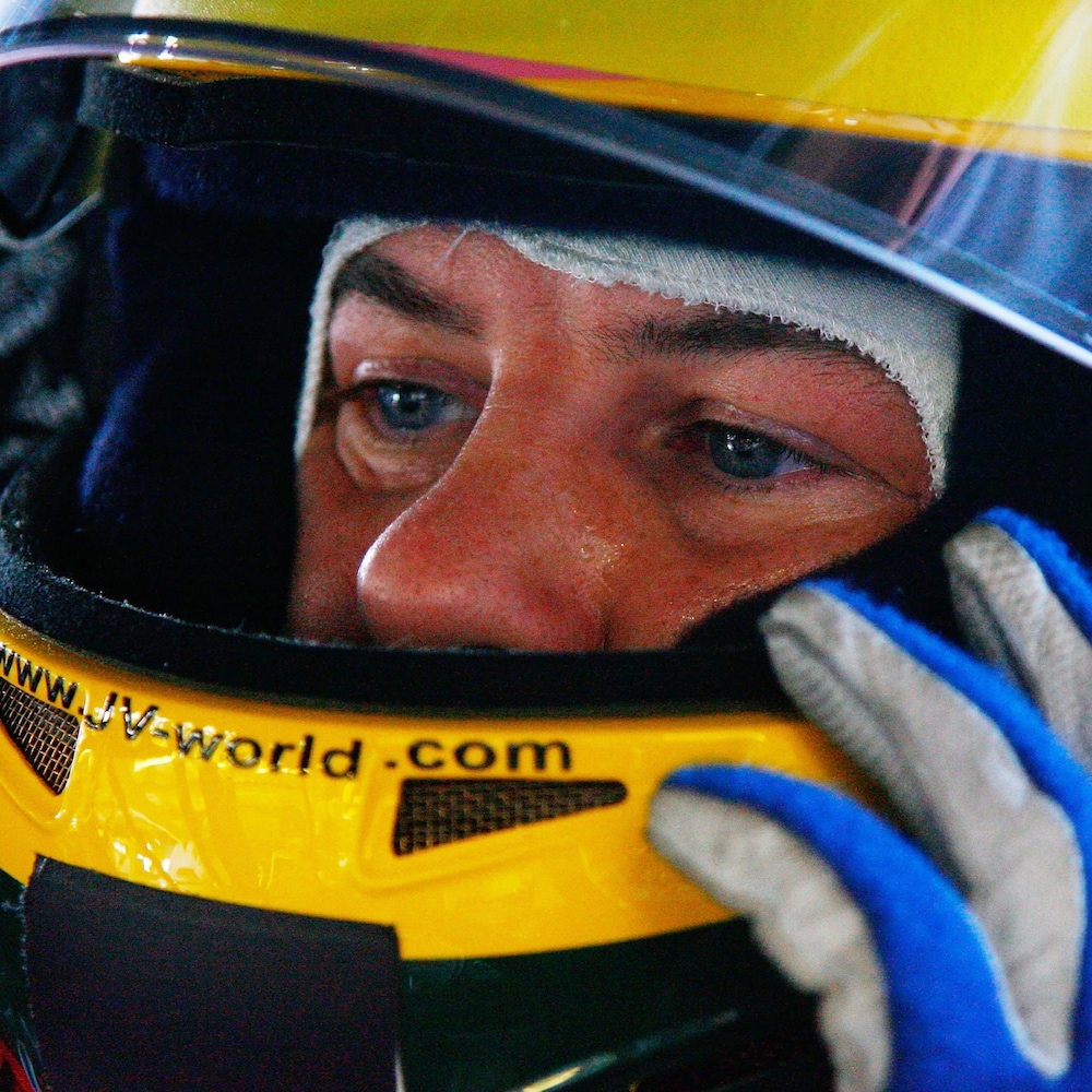 Jacques Villeneuve porte un casque de pilote automobile.