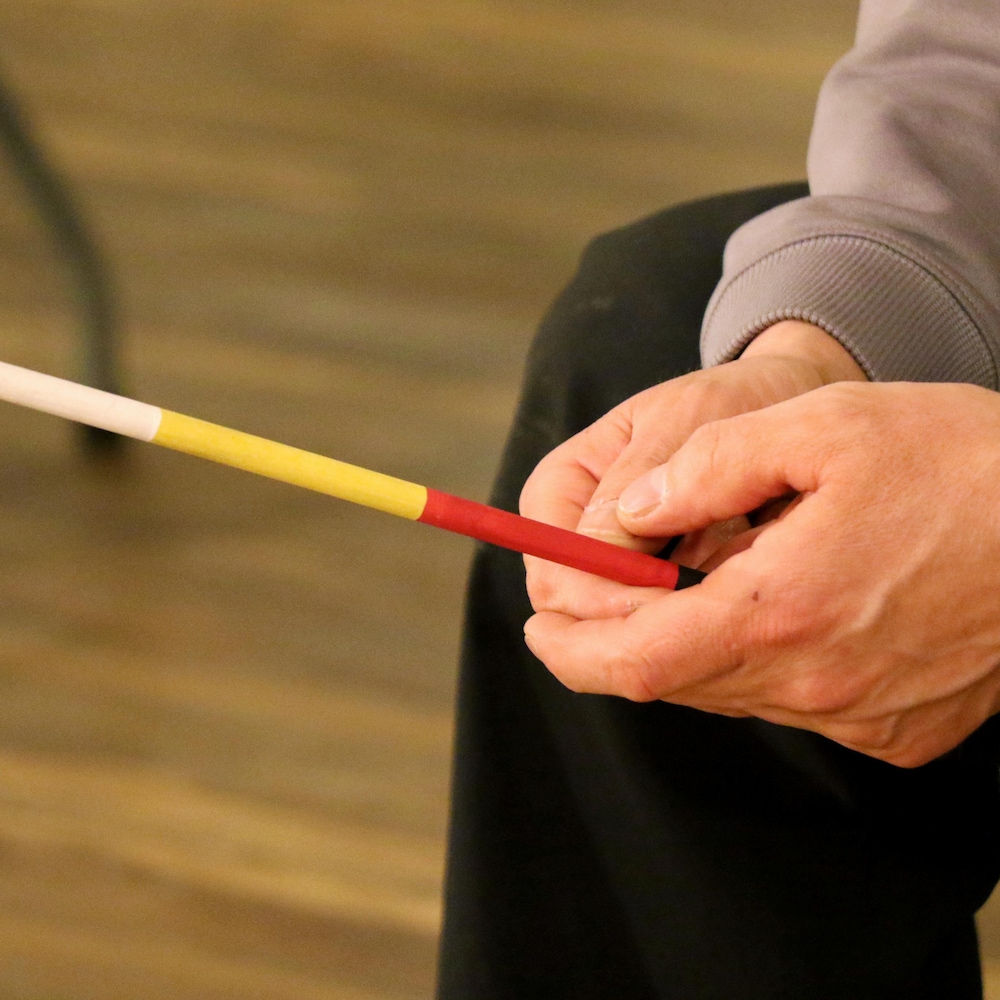 Un homme tient un bâton de couleur blanche, jaune, rouge et noire.