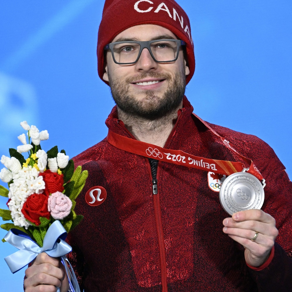 Laurent Dubreuil pose fièrement avec sa médaille d'argent dans une main et un bouquet de fleurs dans l'autre. 