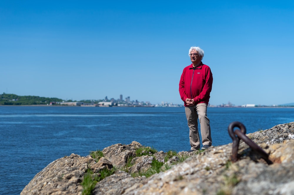 Le photographe et historien Pierre Lahoud est debout sur un massif de roches, près de l'eau. 