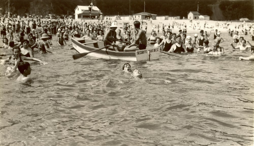 Les sauveteurs de l'anse au Foulon à l'oeuvre en 1938, alors qu'un enfant en ramène un autre à une chaloupe sous les yeux d'une foule nombreuse de baigneurs.