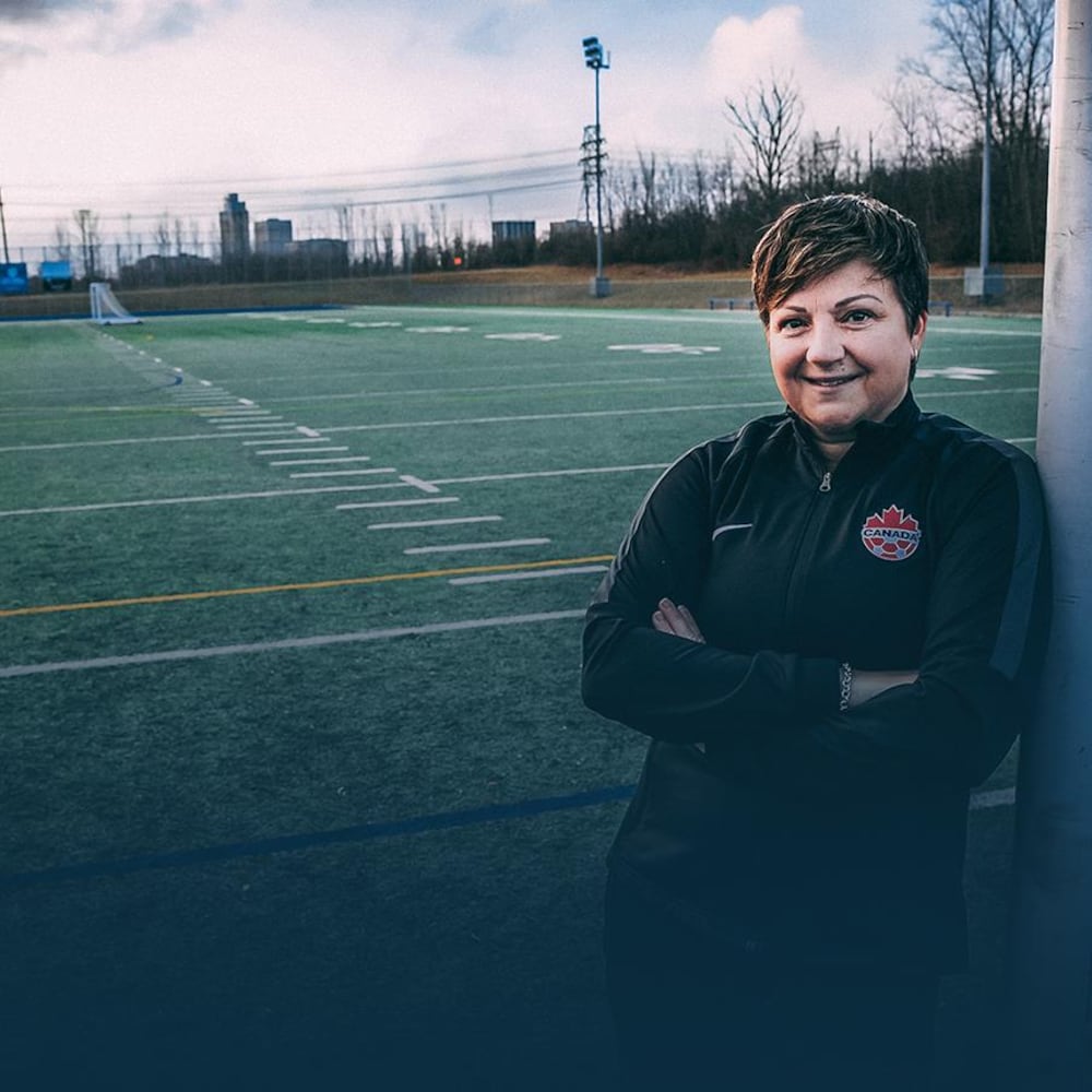 Carol Anne Chénard est appuyée sur un but de soccer et sourit.