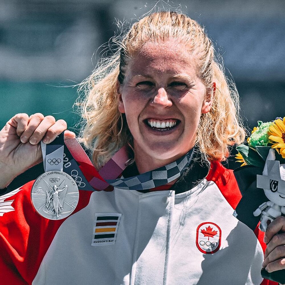 Une femme sourit en brandissant une médaille d'argent.