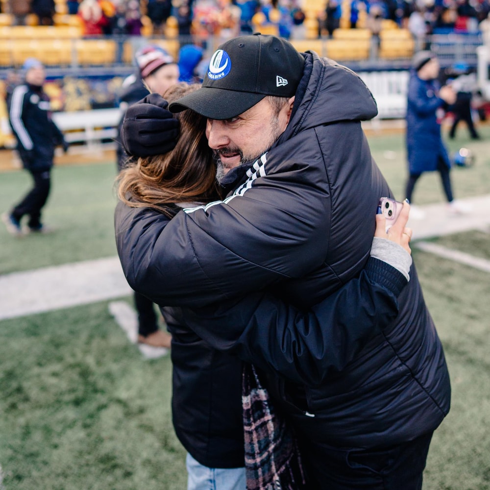 L'entraîneur de football, vêtu de noir, enlace sa fille après une victoire de son équipe. 