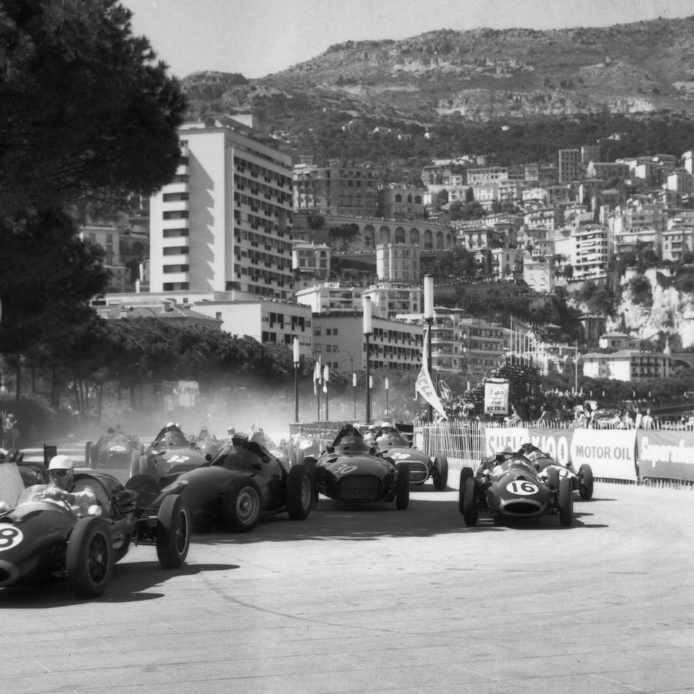 Black and white photo of a race in Monaco in 1958, the cars in front will settle to the right.  We see buildings and mountains in the background