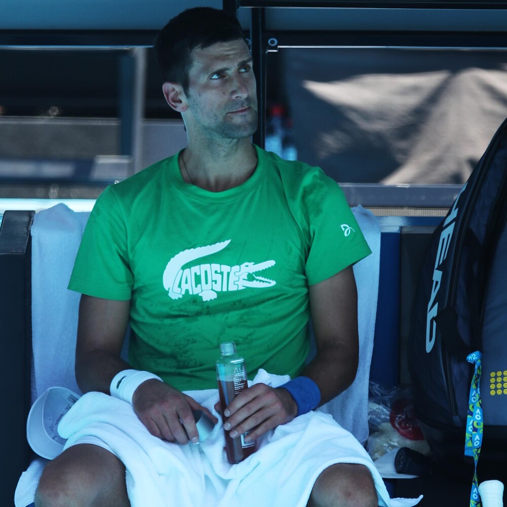 Un joueur de tennis songeur est assis à l'ombre avec une bouteille à la main.