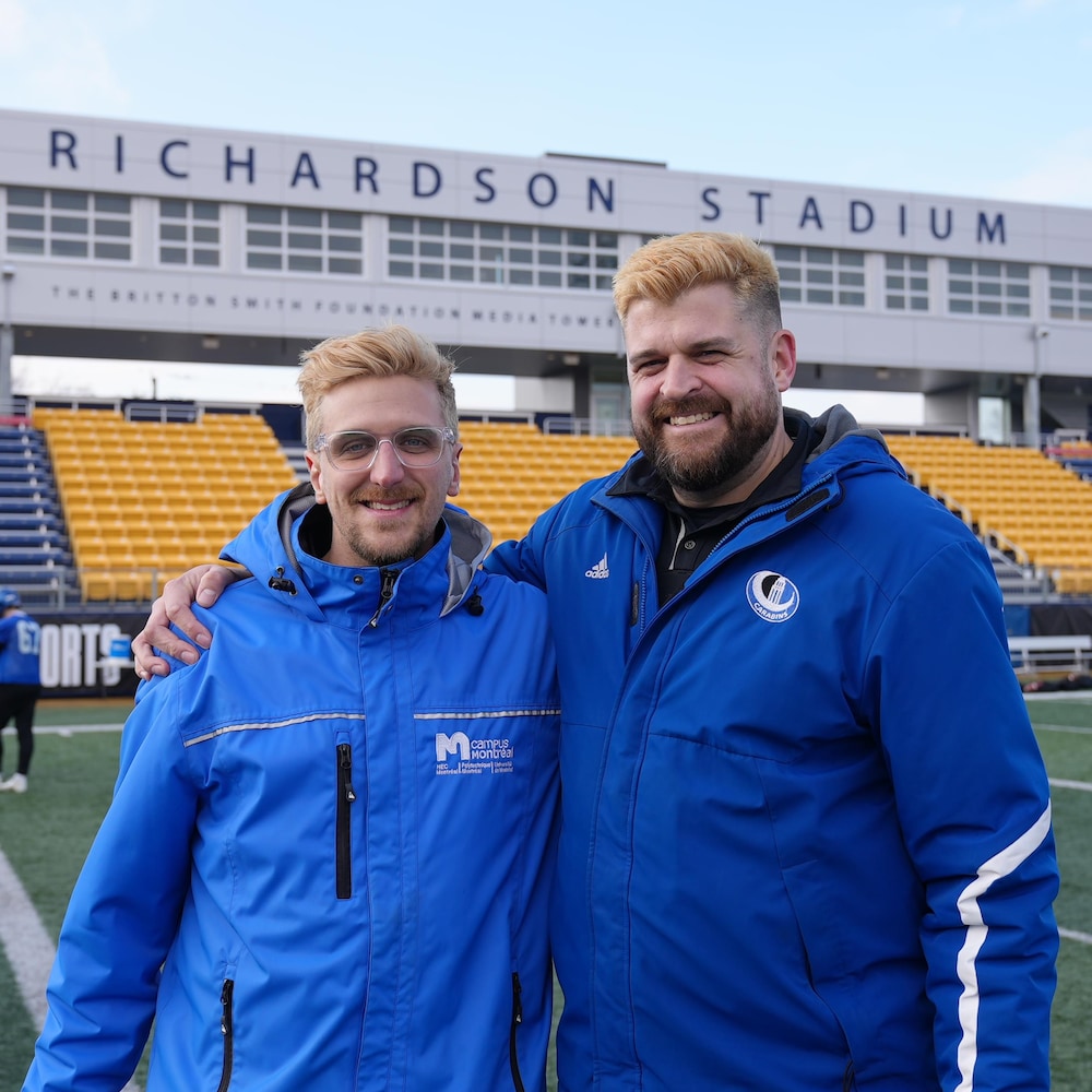 Deux hommes aux cheveux peroxydés avec des manteaux bleus sur un terrain de football.