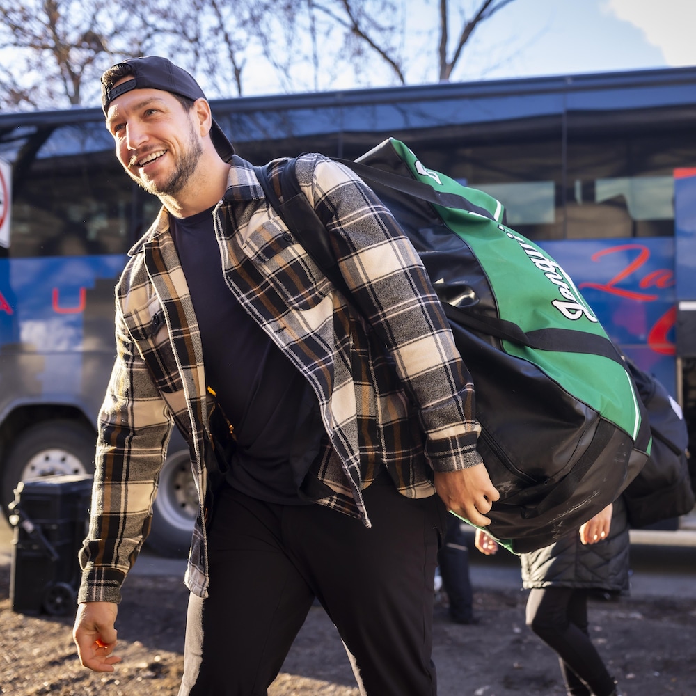 Un joueur de hockey marche avec son sac d'équipement après être sorti d'un autobus. 