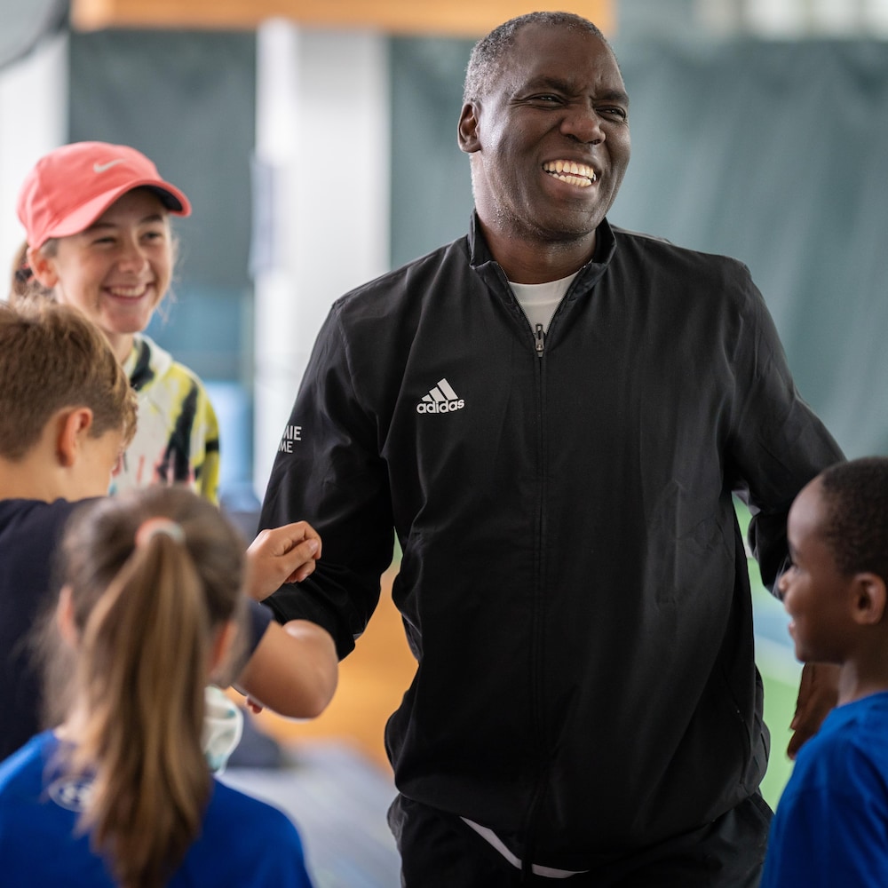 Un homme sourit entouré d'enfants près d'un terrain de tennis