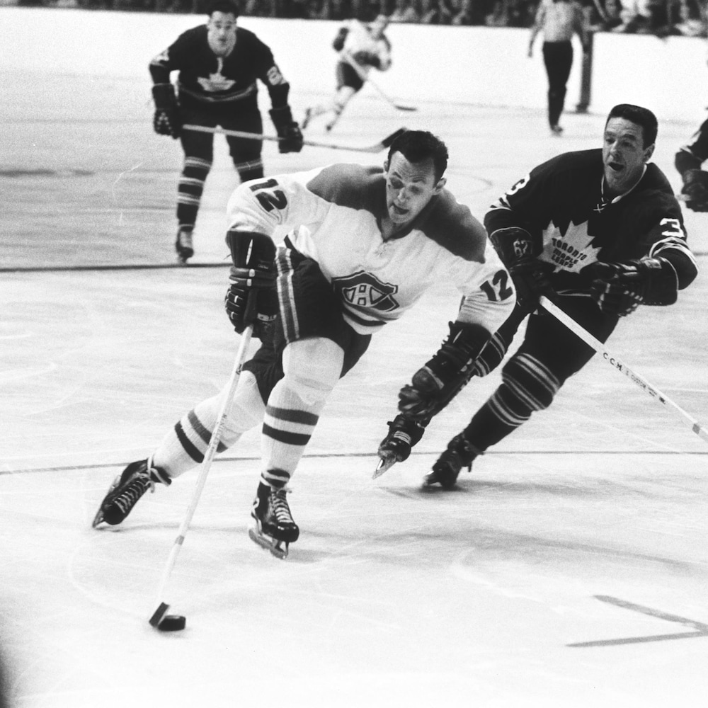 Photo en noir et blanc d'un joueur de hockey qui patine avec la rondelle avec un adversaire à ses trousses.