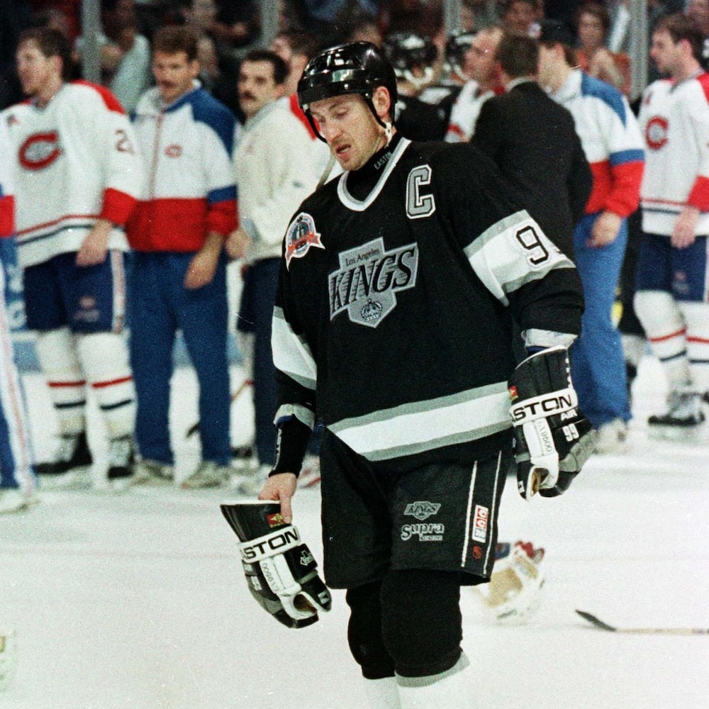 Un joueur de hockey a la tête basse et regarde au sol pendant que, derrière lui, les joueurs de l'équipe adverse fêtent sur la patinoire.