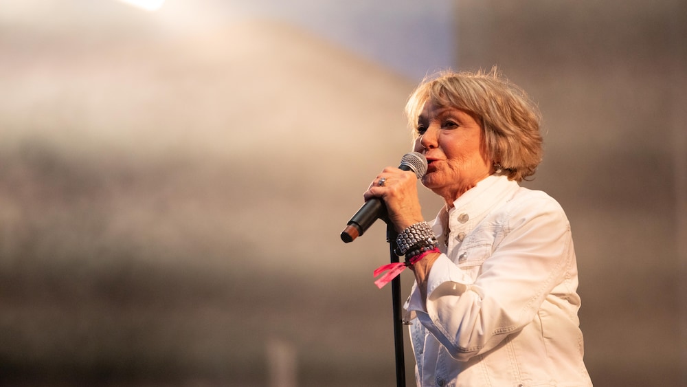 Une femme vêtue de blanc chante sur une scène. 