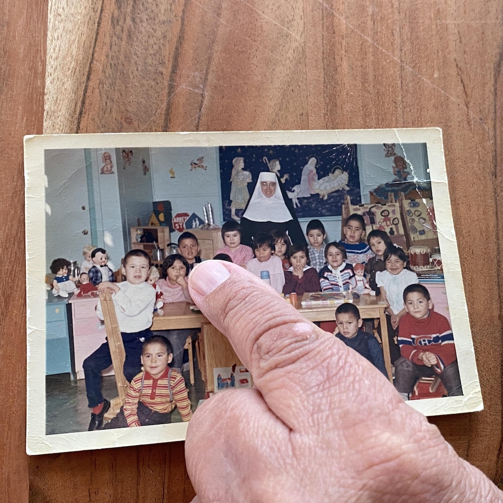 Un doigt montrant un enfant sur une photo de classe avec une religieuse en arrière.