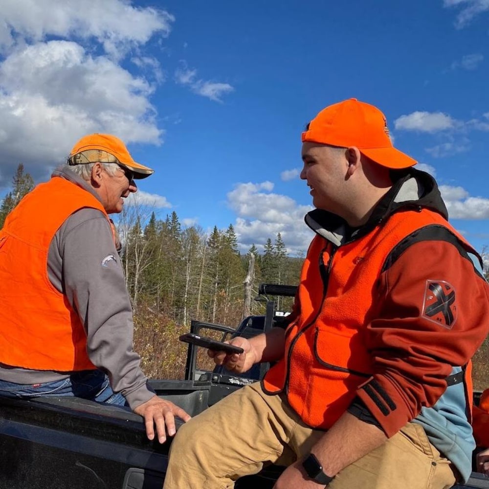 Deux hommes vêtus de dossards de chasseurs prennent place à l'arrière d'une camionnette.