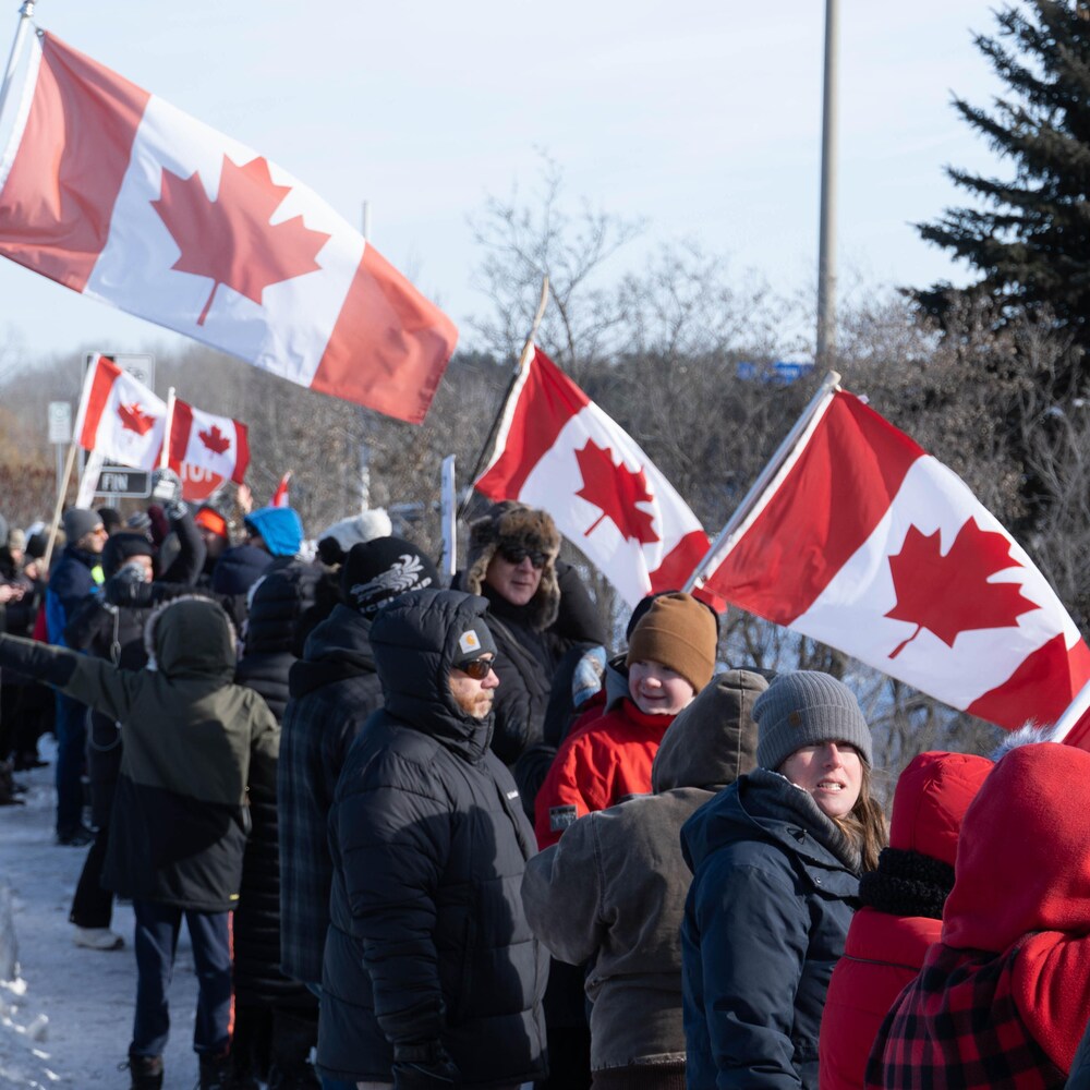 Des personnes brandissent le drapeau canadien et des pancartes sur un viaduc en hiver.