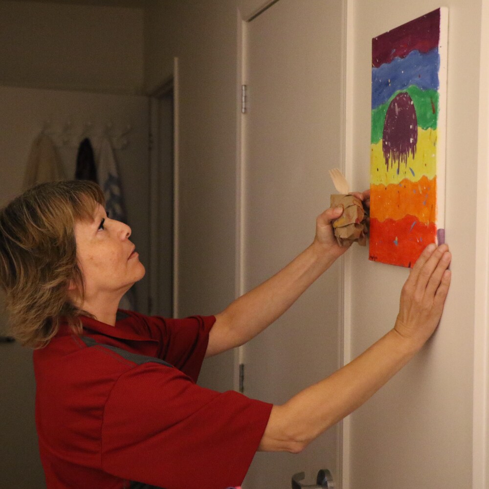 Une femme appose une peinture sur un mur.