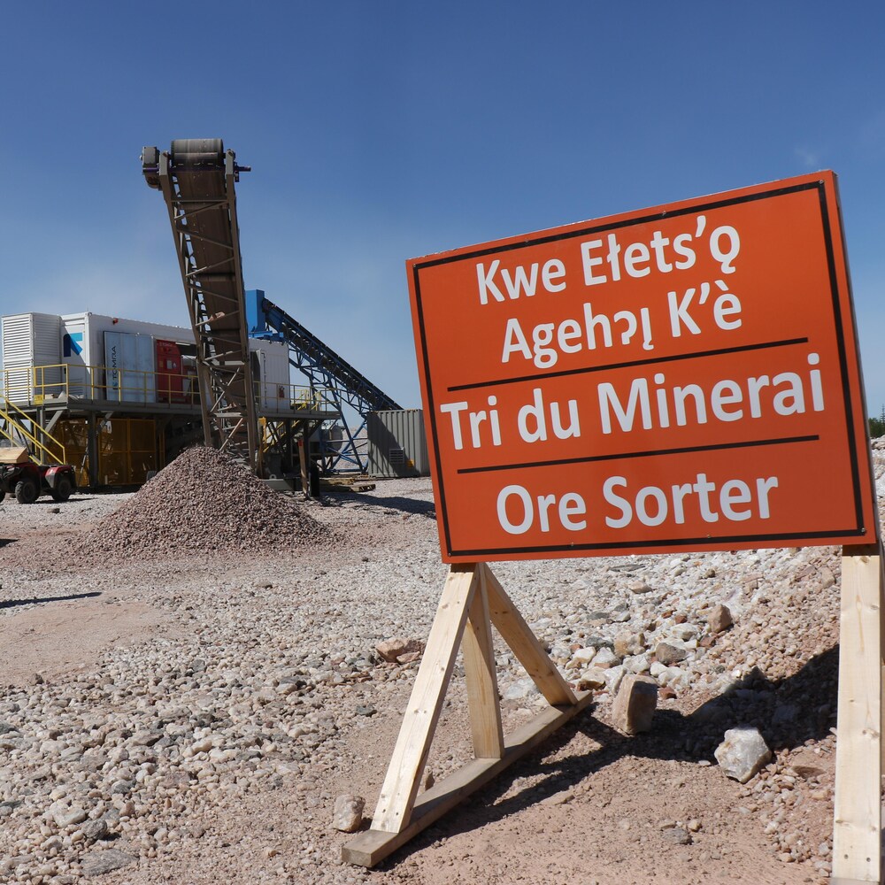 Deux hommes devant une machine qui trie les minerais et un panneau avec l'inscription tri du minerai en trois langues