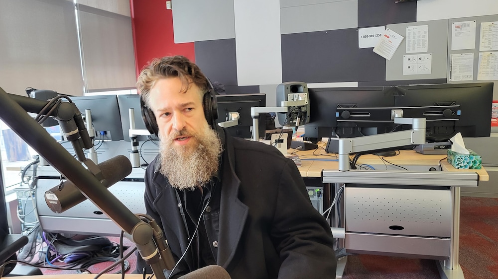Un homme barbu vêtu de noir dans un studio de radio.