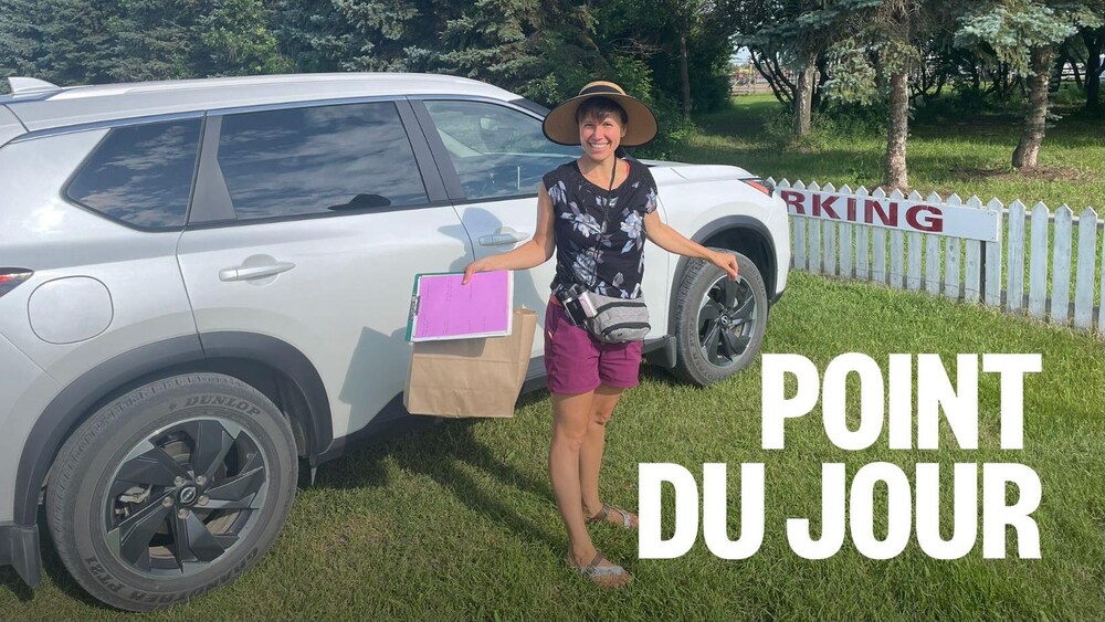 Une femme se tient debout dans un jardin devant un véhicule, tenant des feuilles annotées à la main.