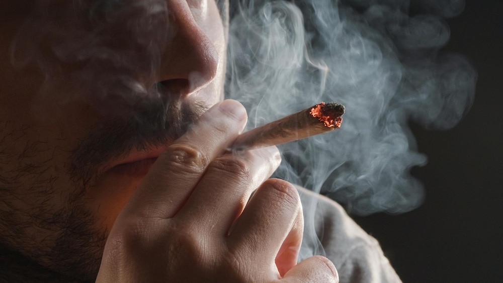 Un homme en train de fumer un joint de cannabis.