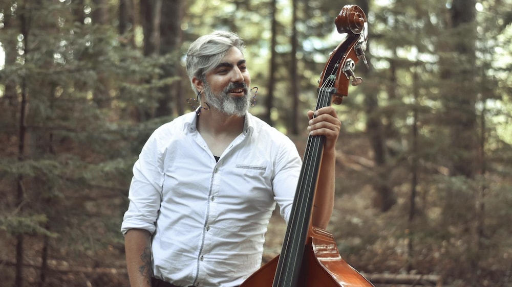 Corey Thomas tient sa contrebasse d'une main dans un décor forestier.