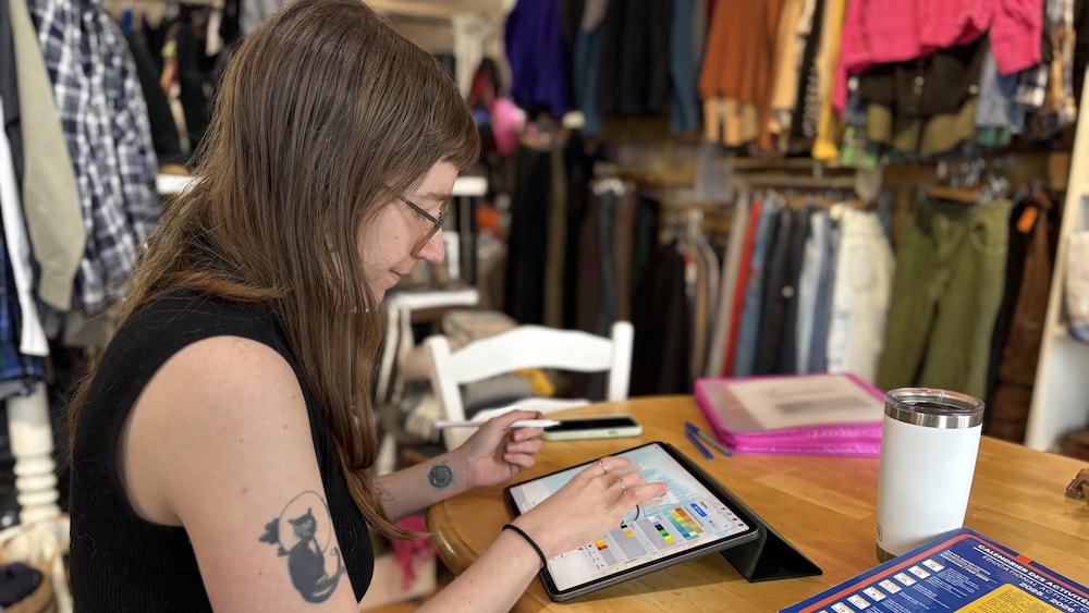 Une femme en train de travailler sur nue tablette graphique. Il y a des vêtements en arrière-plan.
