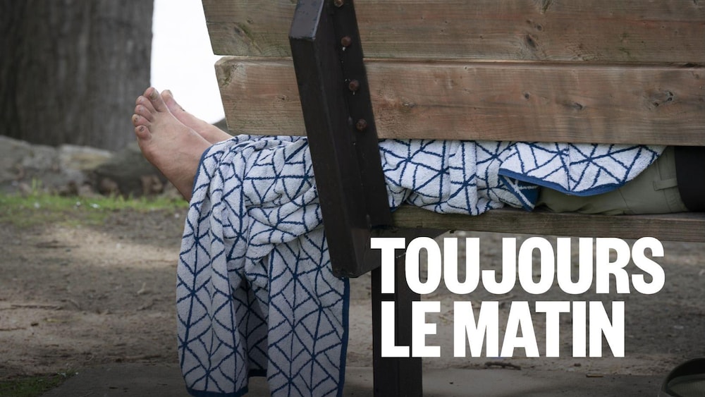 Gros plan sur les pieds nus d'une personne en situation d'itinérance couchée sur un banc public. 