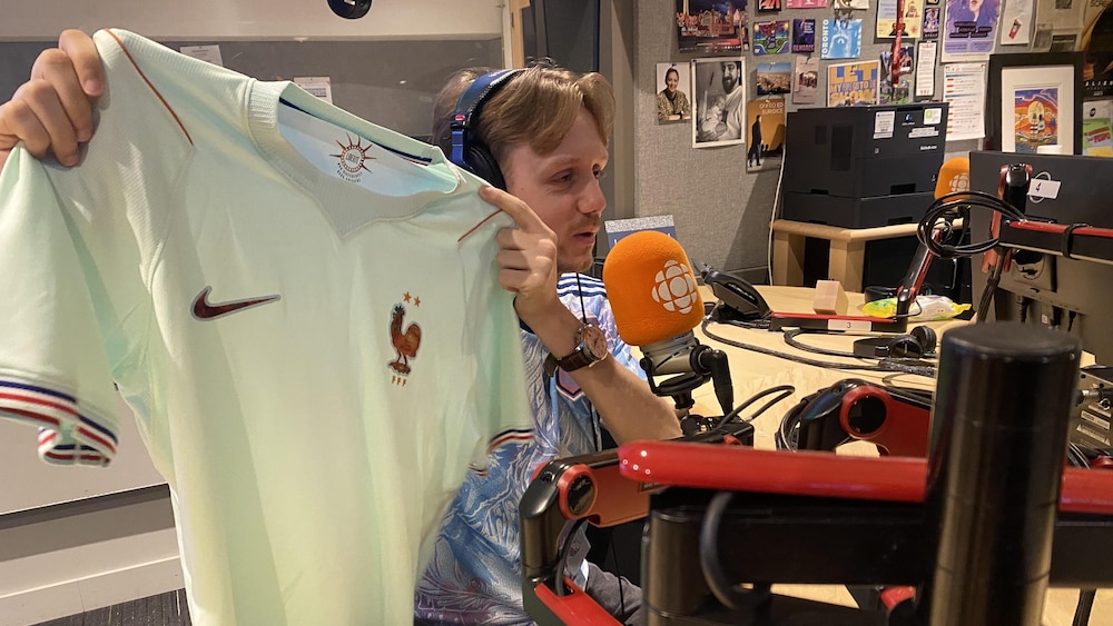 Léo Molinié tient un maillot de soccer de l'équipe de France et parle dans un micro.