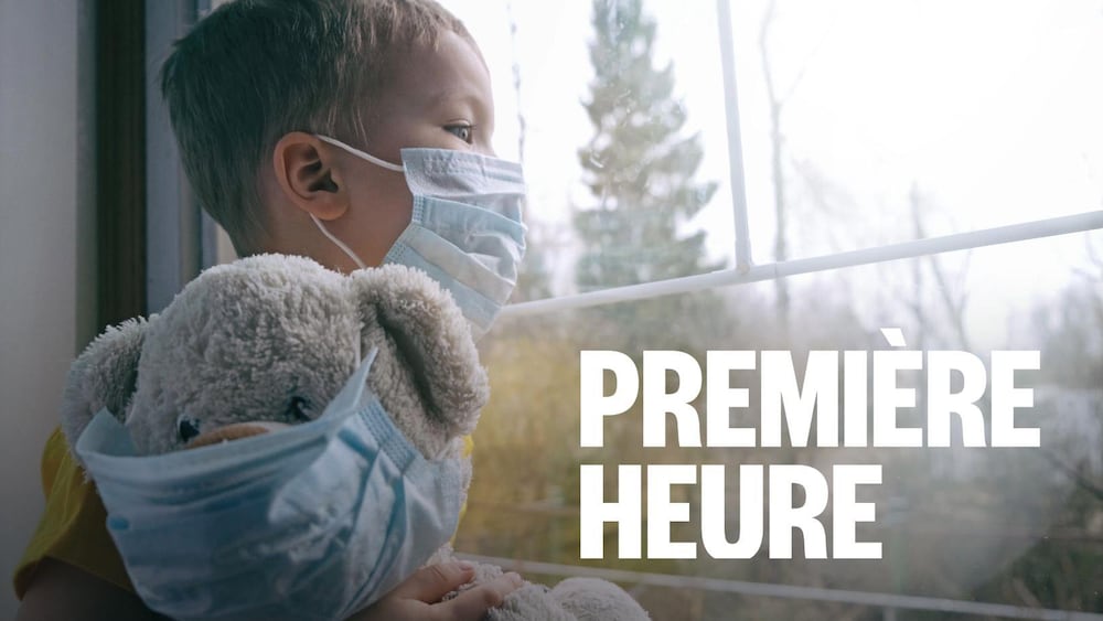 Un enfant avec un masque regarde par la fenêtre avec son toutou.