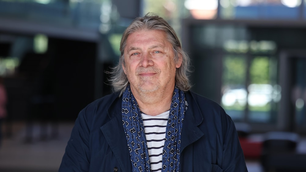 Michel Jean regarde la caméra, en souriant légèrement.