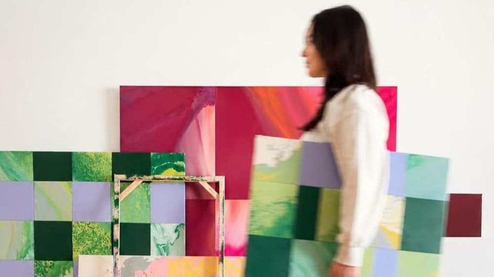 Une femme qui passe devant des tableaux, en portant une toile.