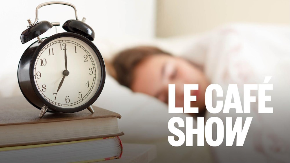 Une adolescente dort dans un lit blanc. Réveil au premier plan sur une pile de livres.