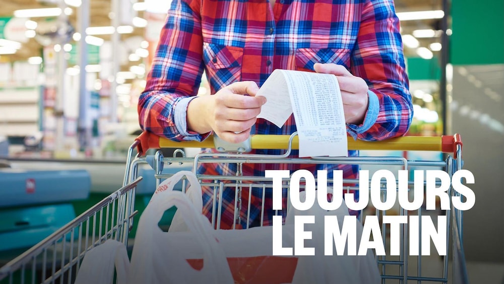 Une personne appuyée sur un panier d'épicerie tient un reçu d'achat.