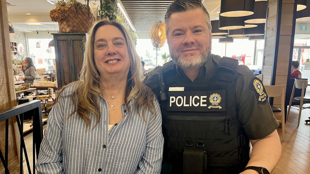 Une femme et un policier sourient à la caméra à une table de café.